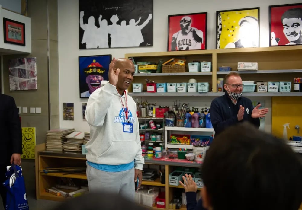 The basketballer Stephon Marbury waves at the front of an art classroom